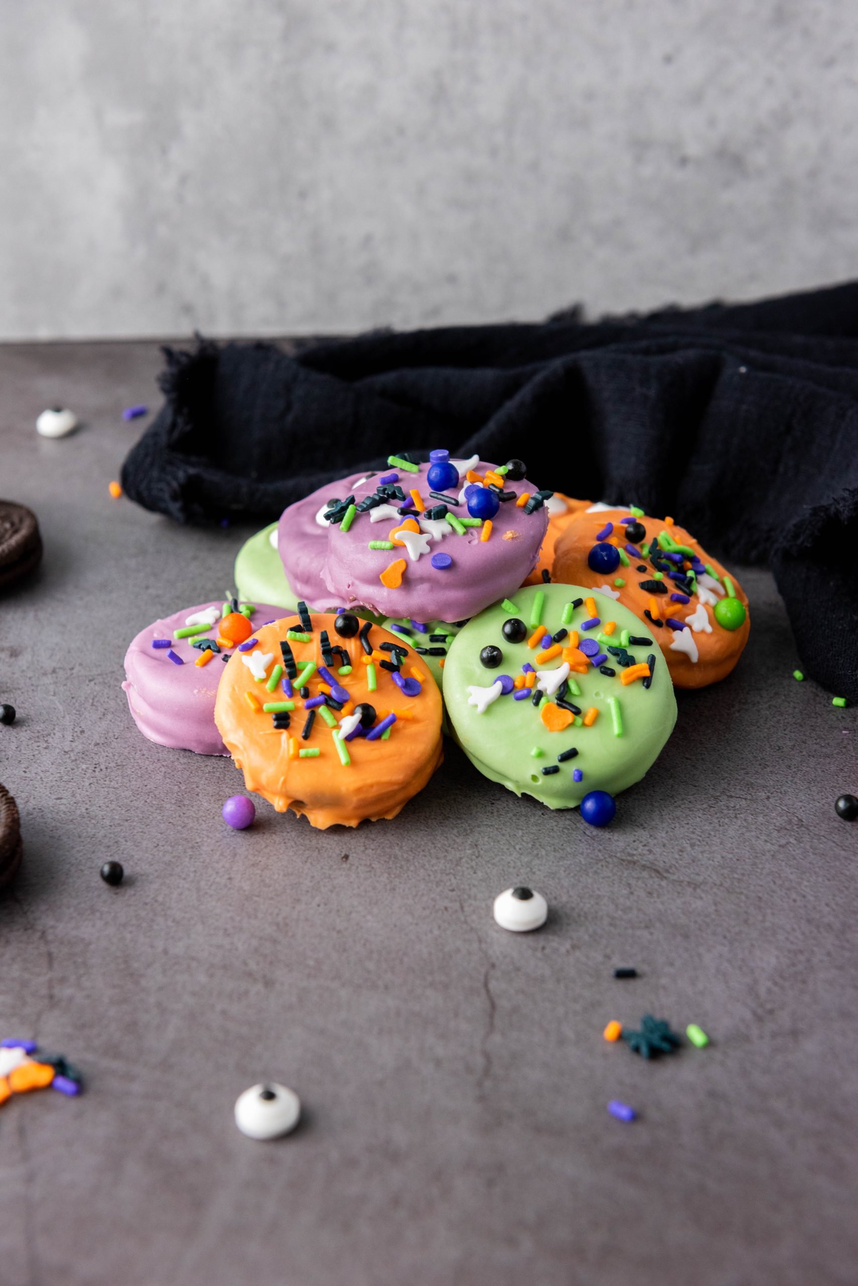 Colorful Halloween Oreos coated in orange, purple, and green candy melts and topped with spooky candy eyes and festive sprinkles.