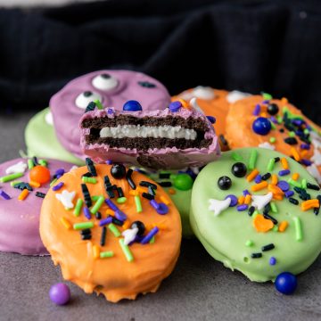 Halloween Oreos dipped in colorful candy melts and decorated with candy eyes and festive Halloween sprinkles.