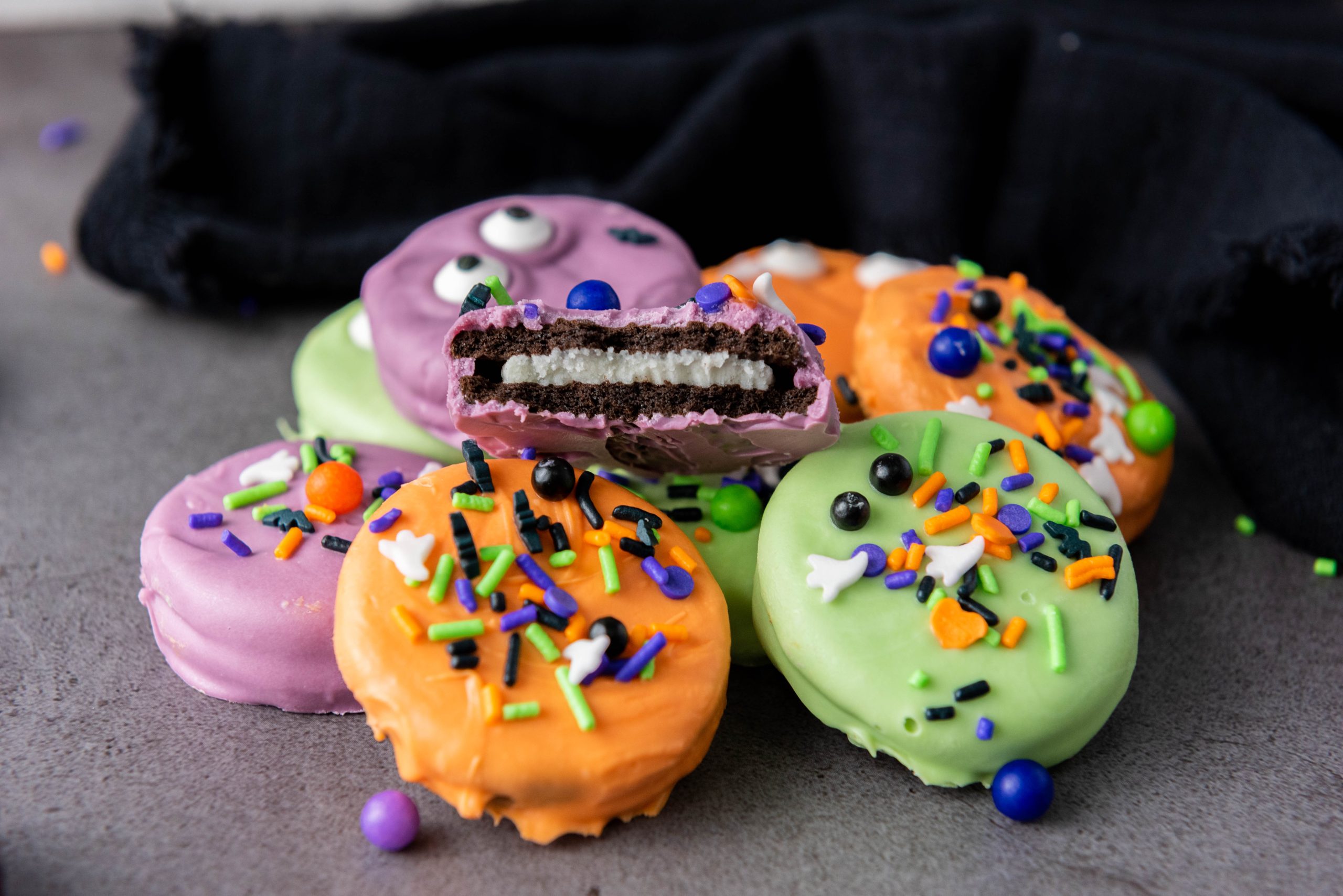 Halloween Oreos dipped in colorful candy melts and decorated with candy eyes and festive Halloween sprinkles.