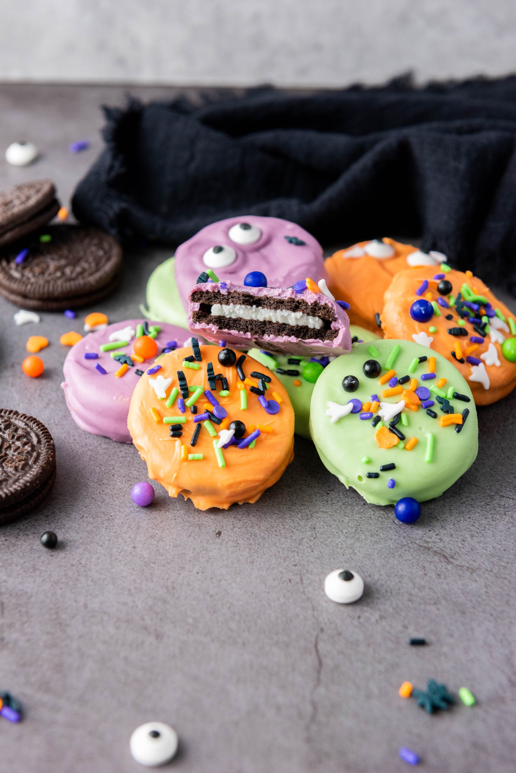Halloween Oreos covered in colorful candy melts and decorated with festive Halloween sprinkles and candy eyes.