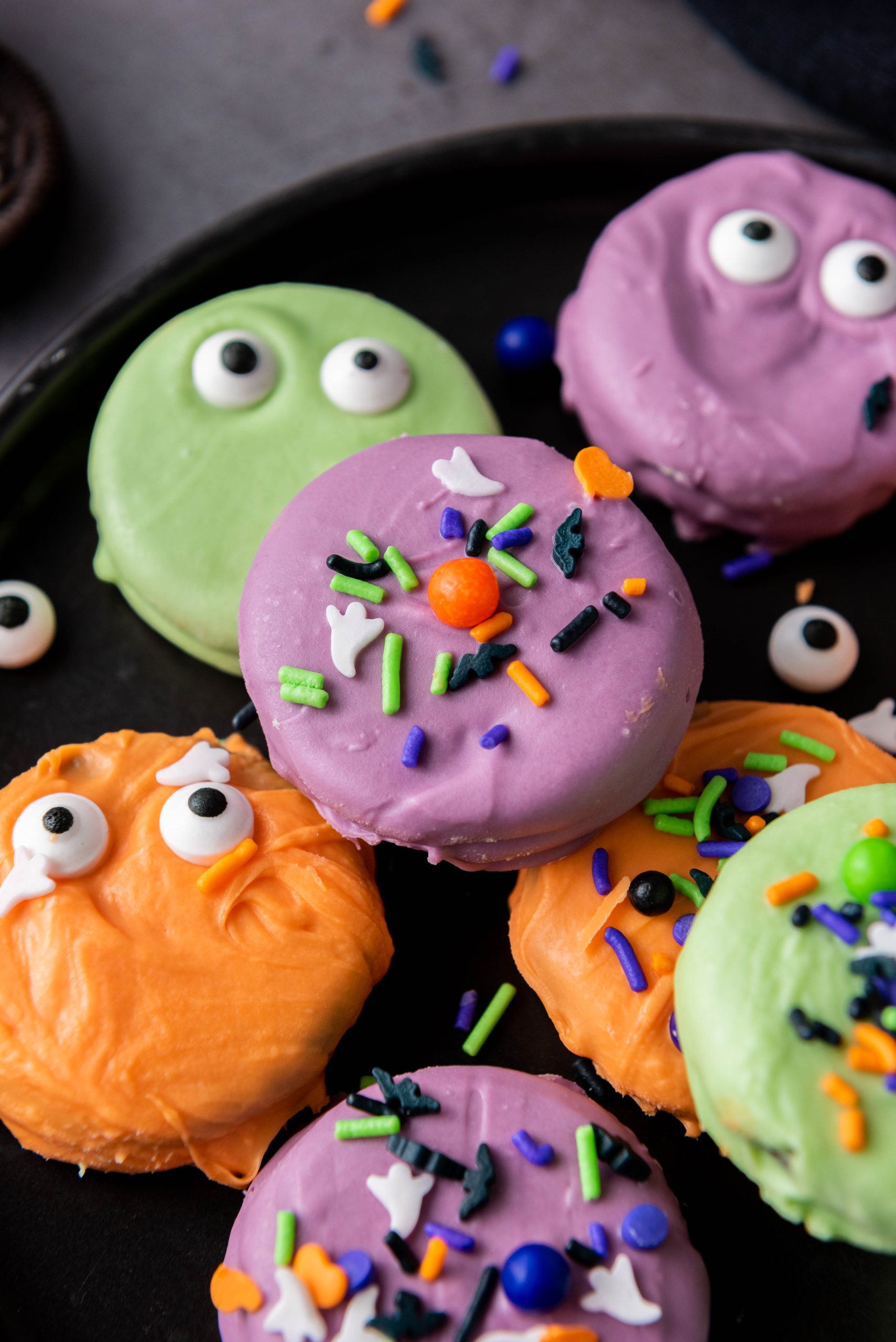 Halloween Oreos decorated with orange, purple, and green candy coating, spooky candy eyes, and colorful Halloween sprinkles.
