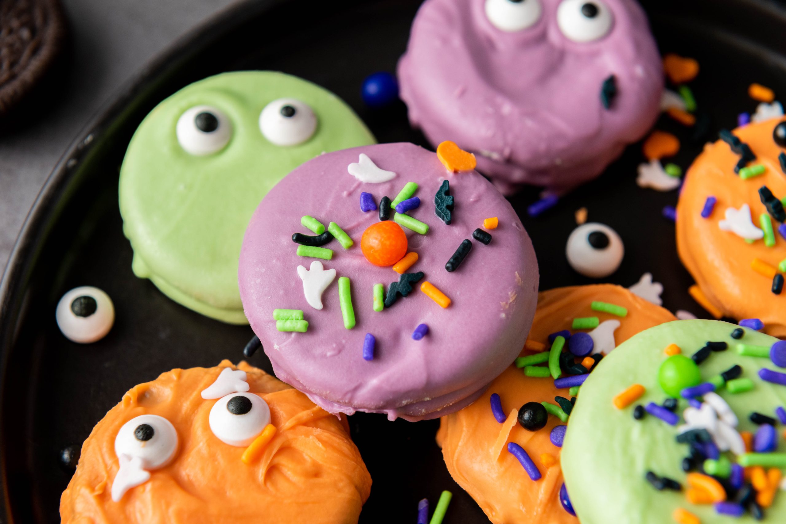 Halloween Oreos dipped in colorful orange, purple, and green candy coating and decorated with spooky candy eyes and festive sprinkles.
