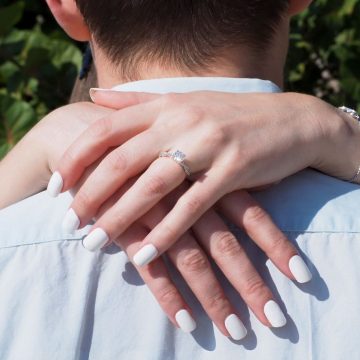 Close-up of a couple embracing, showcasing a diamond engagement ring during a sunny day.