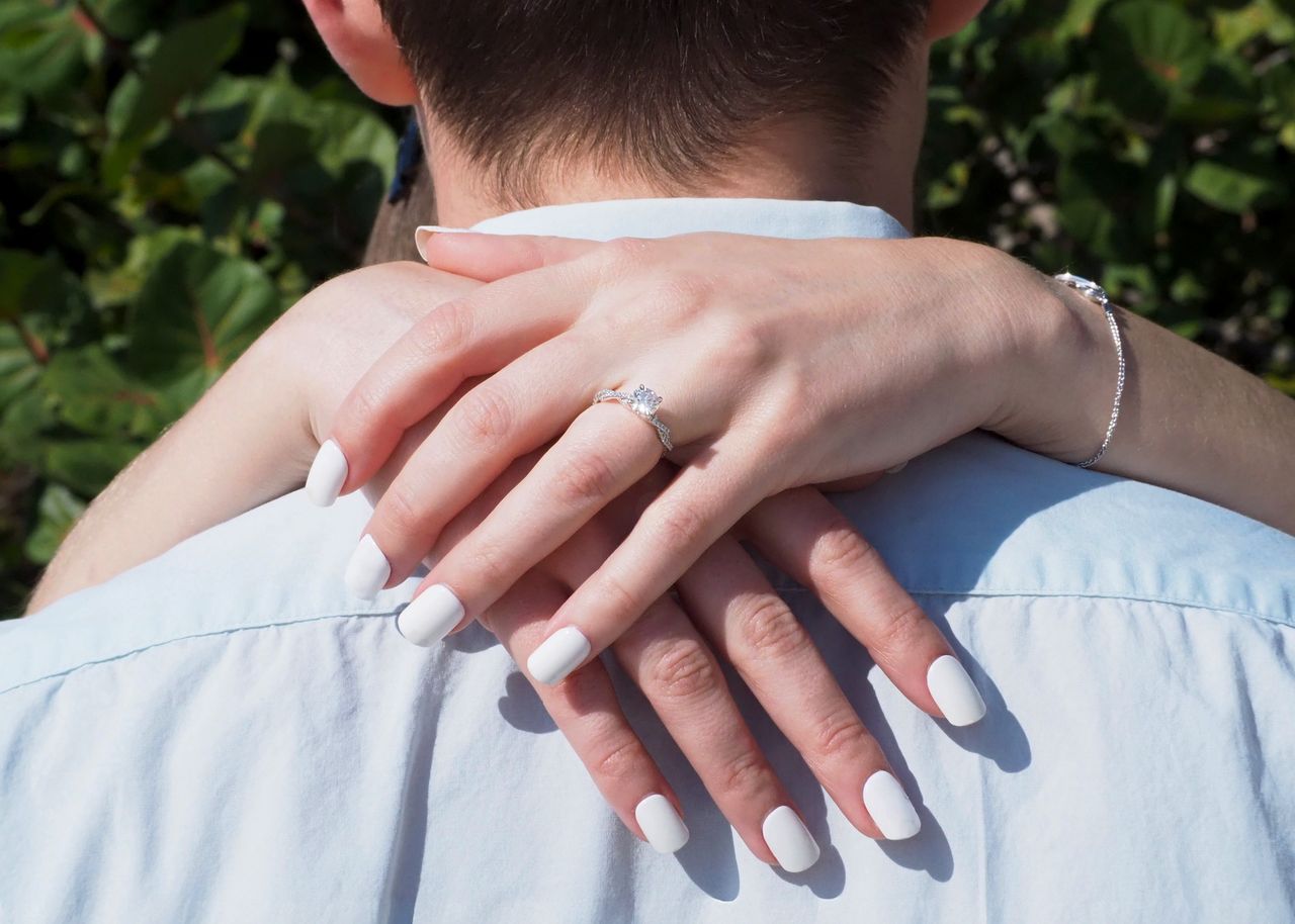 Close-up of a couple embracing, showcasing a diamond engagement ring during a sunny day.