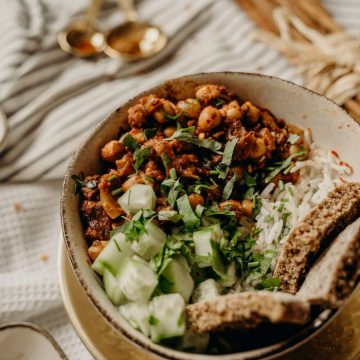 Tasty vegan bowl with chickpeas, rice, cucumber, and herbs on a rustic table.