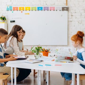 Students and teacher interacting in a bright, colorful classroom setting.