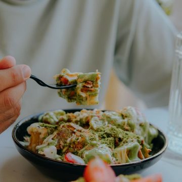 Close-up of a person eating creamy green sauce pasta at a table