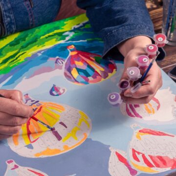 Artist painting colorful hot air balloons on canvas using acrylic paints.