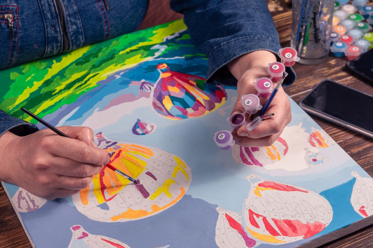 Artist painting colorful hot air balloons on canvas using acrylic paints.